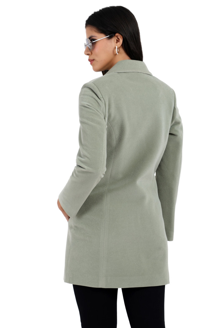 A back pose of a standing woman, wearing Coatsnmore’s rust Semi-Long Velvet coat with a lapel collar, button closure, side pockets and black jeans.